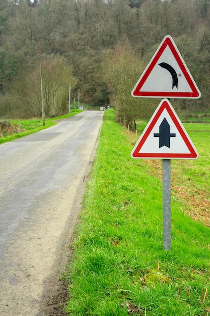 Road and road sign warning about a turn in the road Road safety concept A sign in red triangle indicating a left turn of the road and an intersection sign with a minor road