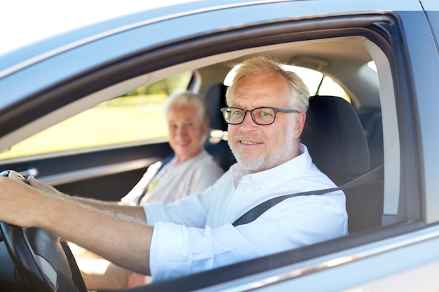 road trip, travel and old people concept - happy senior couple driving in car