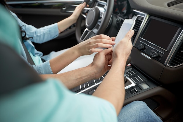 road trip, travel, technology and people concept - happy man and woman with smartphone driving in car