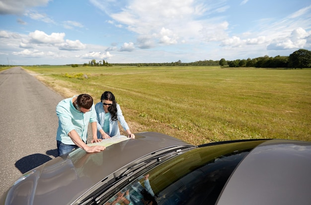 road trip, travel, tourism, family and people concept - happy man and woman searching location on map on car hood outdoors