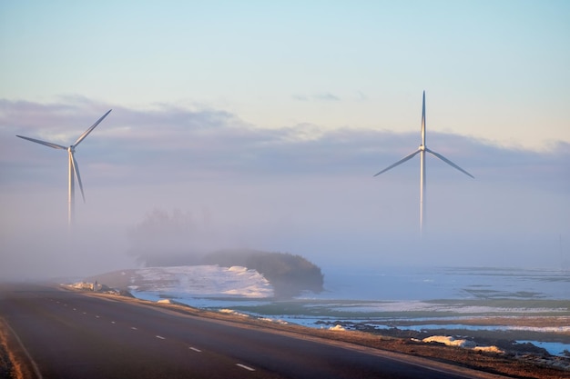 Road to wind power stations half hidden ones in the fog Early during the sunrise in the winter Renewable energy concept