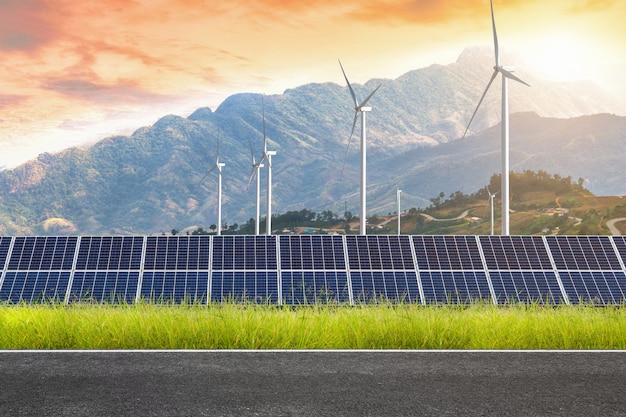 road with solar panels with wind turbines against mountanis landscape against sunset sky