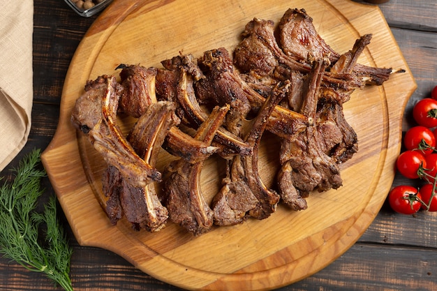 Roast rack of lamb served on wooden board on dark wooden