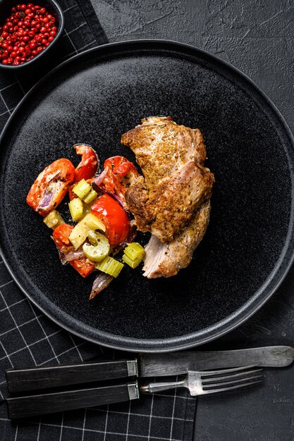 Roast Turkey thigh fillet with vegetables. Black background. Top view