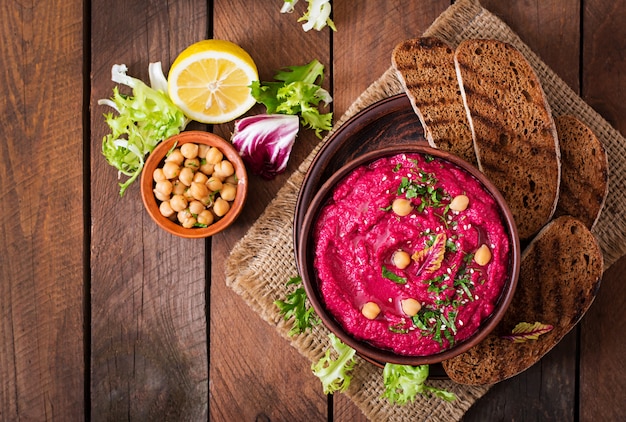 Roasted Beet Hummus with toast in a ceramic bowl on a wooden table. 