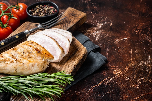 Roasted chicken breast fillet on a wooden board with herbs Dark background Top view Copy space