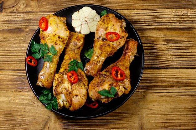 Roasted chicken drumsticks with spices in a black plate on a wooden table Top view