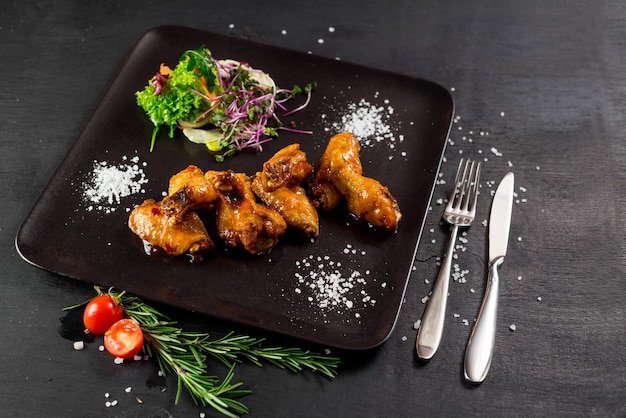 Roasted chicken legs with vegetables on black background