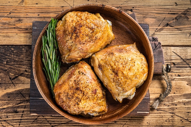 Roasted chicken thighs in a wooden plate with rosemary and herbs