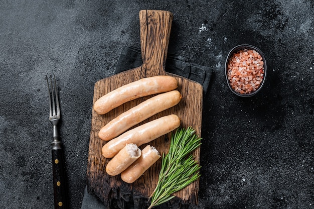 Roasted chicken and turkey sausages on a wooden board. Black background. Top view.