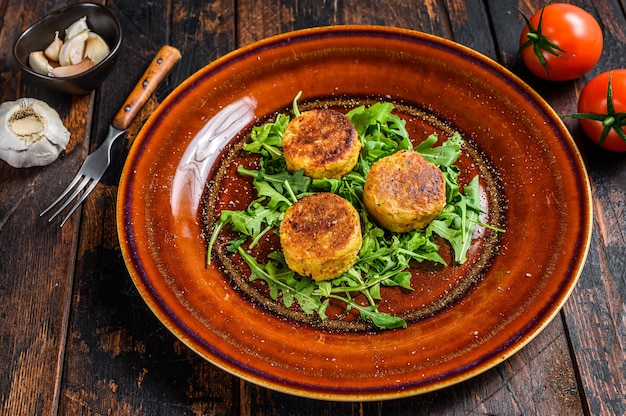 Roasted chickpeas falafel patties with arugula on a plate. Dark wooden table. Top view.