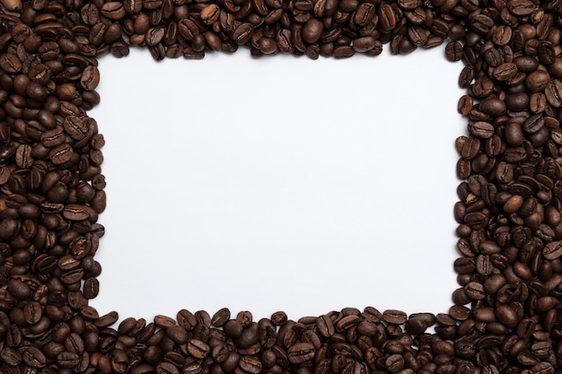 Roasted coffee beans surround a white frame Copy space Top view