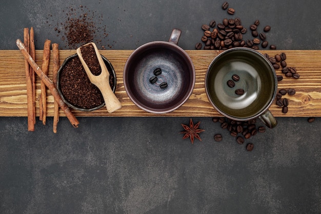 Roasted coffee beans with coffee powder and flavourful ingredients for make tasty coffee setup on dark stone background