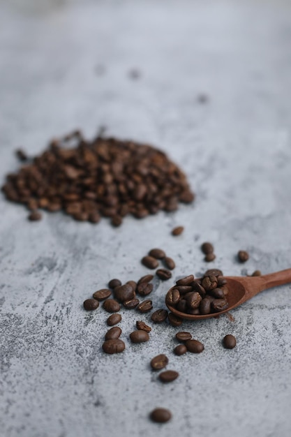 Roasted coffee beans on wooden spoon with blurry image stacks of coffee seeds on gray background