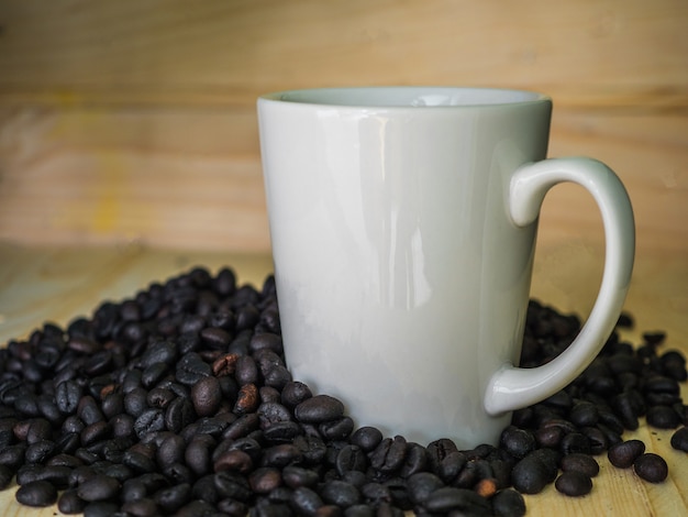 Roasted coffee seed and white cup on wooden background.