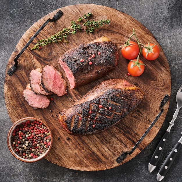 Roasted duck breast on a round wooden board with peppers and cherry tomatoes