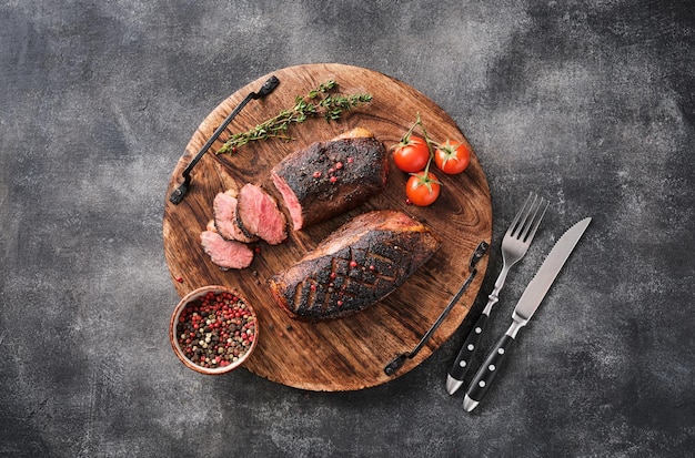 Roasted duck breast on a round wooden board with peppers and cherry tomatoes