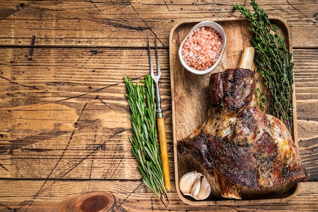 Roasted goat leg meat on a wooden cutting tray. wooden background. Top view. Copy space.