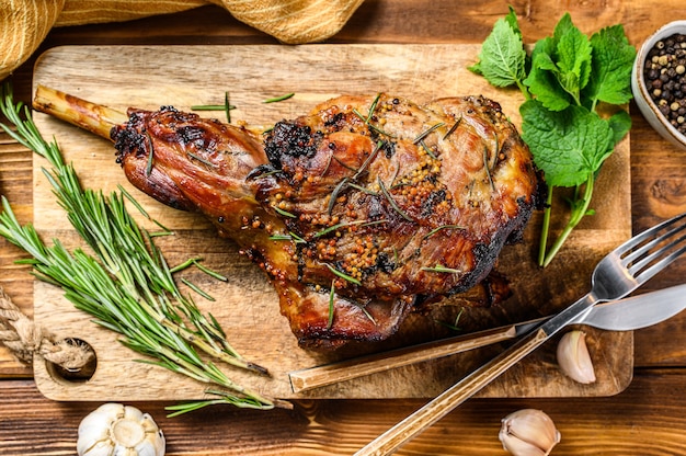 Roasted goat leg with herbs. Farm meat. Wooden background. Top view. Copy space.