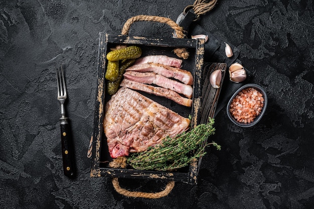 Roasted on grill Pork steaks from neck meat in wooden tray with herbs Black background Top view