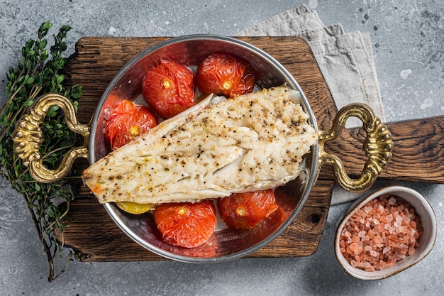 Roasted Haddock fish fillet in skillet with tomato and potato Gray background Top view