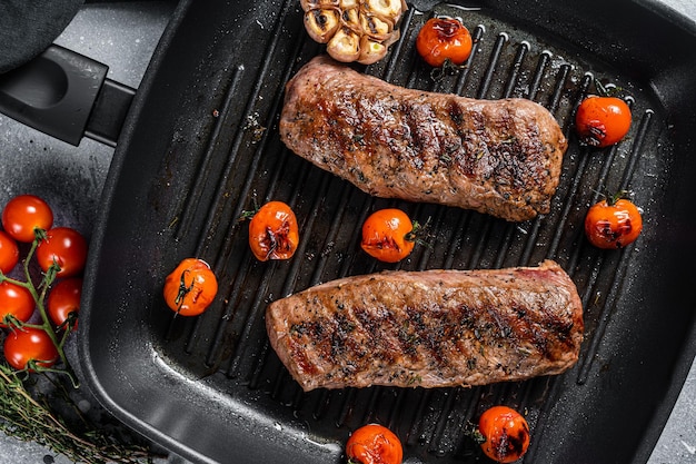 Roasted Lamb tenderloin fillet meat on grill pan, mutton sirloin steak. Gray background. Top view.