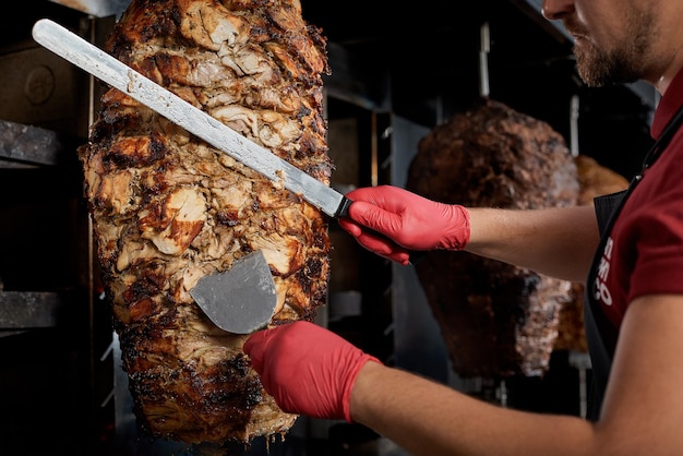 Roasted meat on the bone for the preparation of donors or shawarma Closeup The cook cuts the meat fried over charcoal for the preparation of shawarma in pita breadCloseup