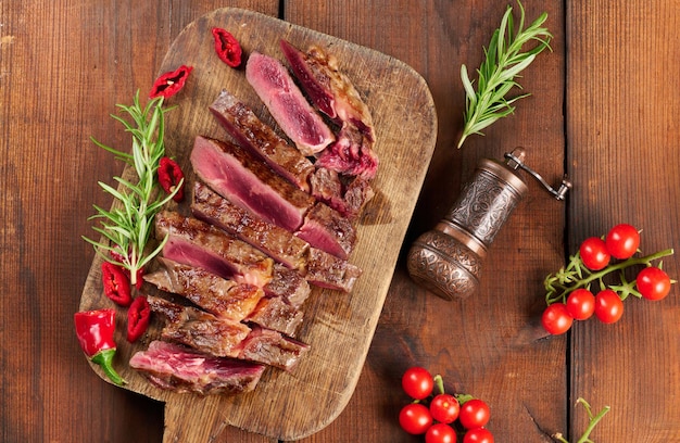 Roasted piece of beef ribeye cut into pieces on a vintage brown chopping board, rare doneness. Delicious steak, top view