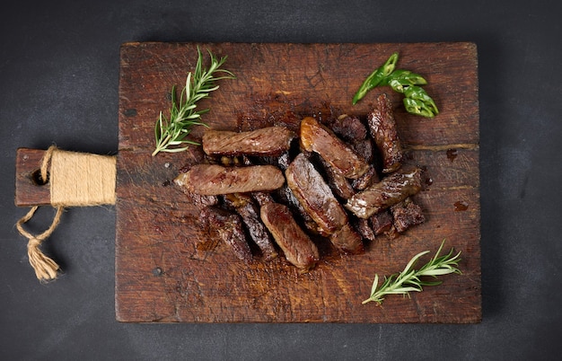 Roasted piece of beef ribeye cut into pieces on a vintage brown chopping board. Well done. Appetizing steak , top view