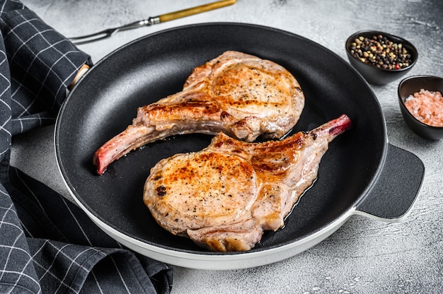 Roasted pork chop meat steak in a pan. White background. Top view.