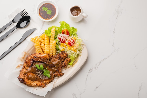 Roasted pork chop steak with salad and spicy sauce on white table background