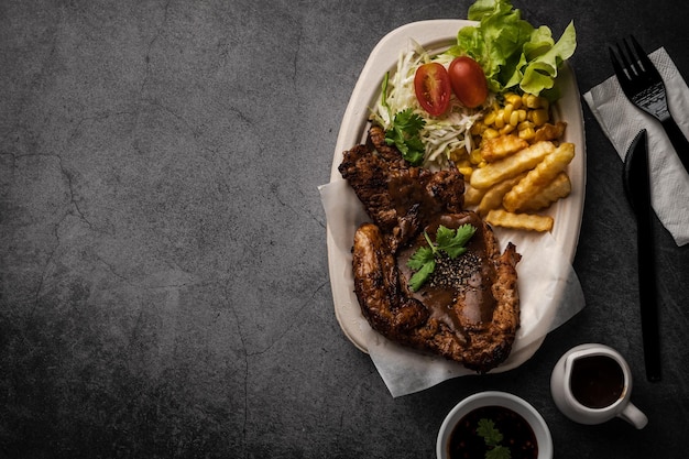 Roasted pork chop steak with spices and rosemary on black plate on wooden background