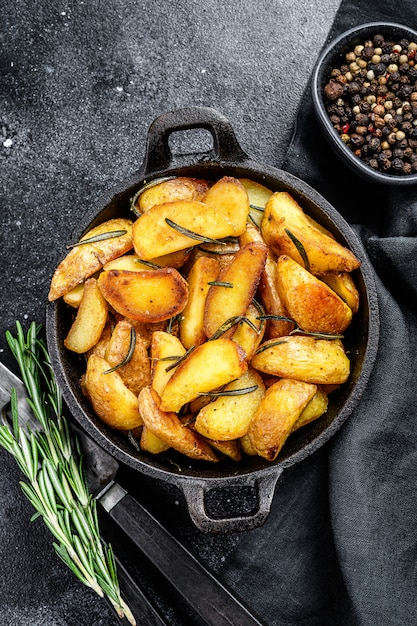 Roasted potato wedges with herbs and rosemary. Black background. Top view