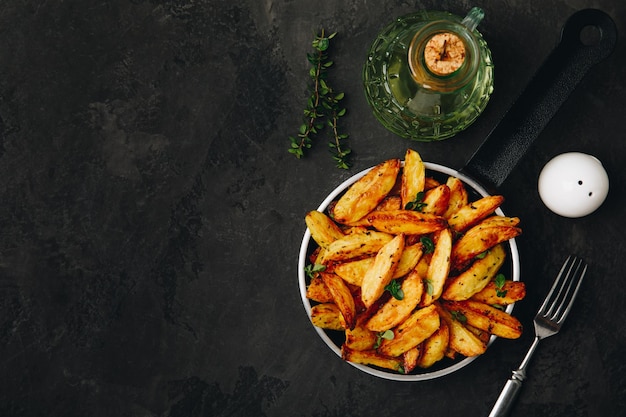 Roasted potatoes Baked potato wedges in frying pan on dark stone background