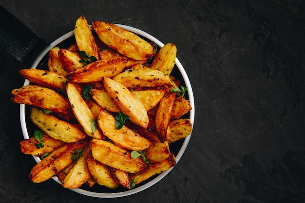 Roasted potatoes Baked potato wedges in frying pan on dark stone background