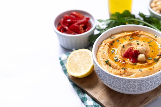 Roasted red pepper hummus in white bowl on white marble background