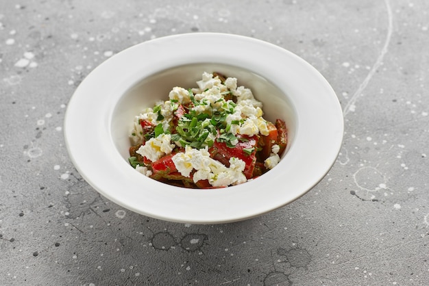 Roasted red sweet peppers and Basil with feta cheese, on a light stone surface.