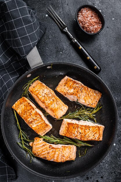 Roasted Salmon Fillet Steak in a pan with rosemary. Black background. Top view.