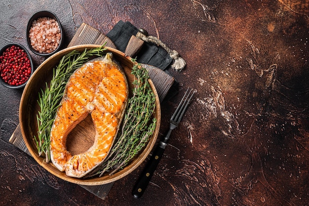 Roasted Salmon Trout Fish Steak in a vintage wooden plate with thyme and rosemary. Dark background. Top view. Copy space.