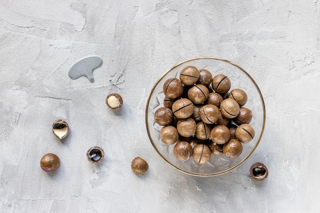 Photo roasted salted macadamia nuts in shell in bowl and opener on gray background concept of health