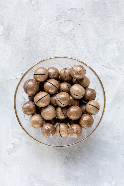 Roasted salted macadamia nuts in shell in glass bowl on gray background, concept of healthy eating vegan food. Top view