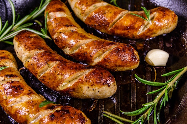 Roasted sausages with rosemary twigs and garlic in a cast iron grill pan