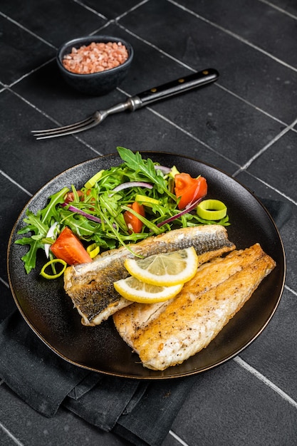 Roasted sea bass fillet with salad Branzino fish Black background Top view