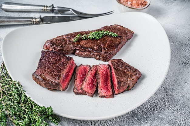 Roasted sliced rump beef meat steak on a plate with thyme. White background. Top view.