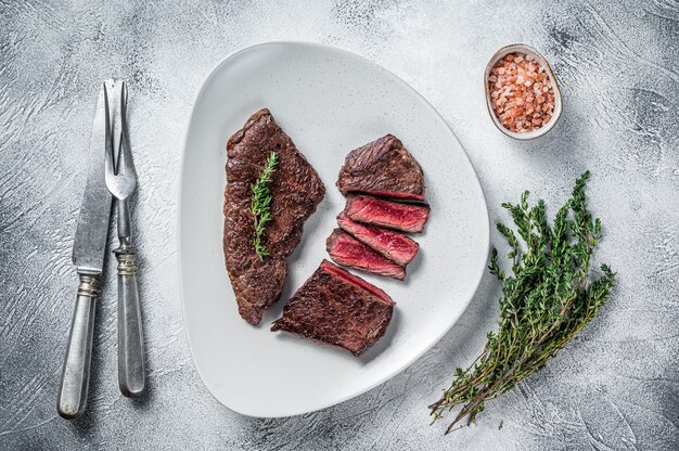 Roasted sliced rump beef meat steak on a plate with thyme