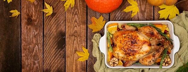 Roasted turkey garnished with cranberries on a rustic style table decorated with pumpkins, orange, apples and autumn leaf