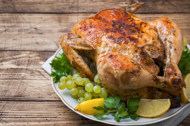 Roasted whole chicken with lemon and grapes on wooden table