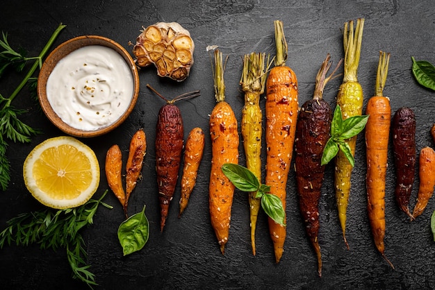 Roasted young whole colorful carrot with herbs over black background top view