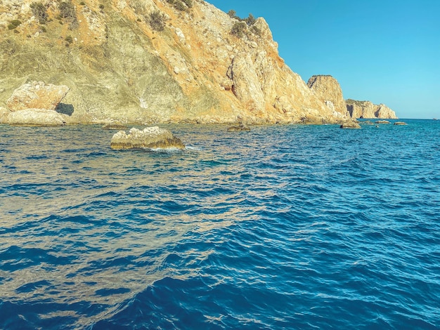 Rock in the center of the sea blue water with bubbling foam with a large high mountain