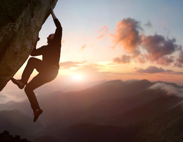 Rock climbing. Male climber trying staying on challenging rock, overcoming obstacles. Mountain and sunrise on background